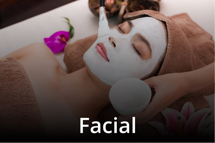 Close-up of a woman receiving a facial with her face covered in white mask, as a technician applies treatment with a brush